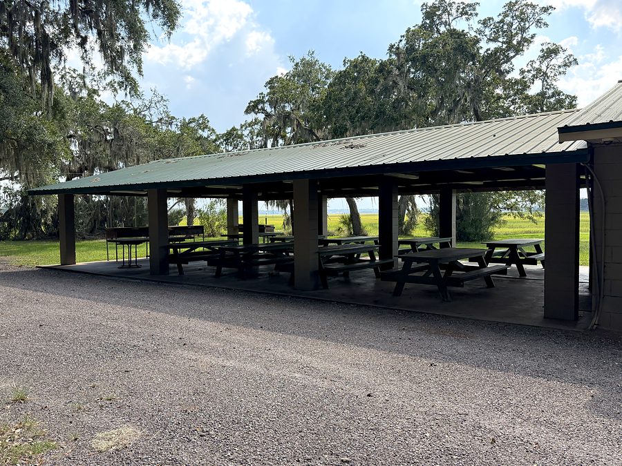 The covered pavilion seen from the parking area, open on all sides, picnic tables beneath, marsh and water beyond